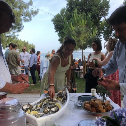 Présentoir en forme de bateau blanc rempli d'huîtres fraîches sur glace et citrons lors d'un cocktail de mariage en extérieur. Invités se servant au buffet de Dimanch'Huîtres au bord de l'eau en Gironde.