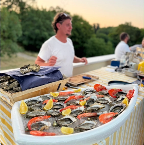 Écailler professionnel de Dimanch'Huîtres animant un bar à huîtres en plein air au Cap Ferret. Présentation premium de fruits de mer, huîtres et crevettes sur un plateau en forme de barque lors d'une réception sur le Bassin d'Arcachon.