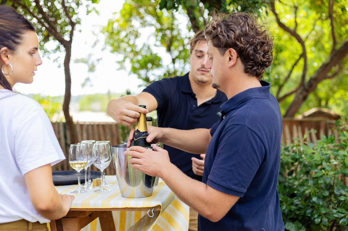 Membres de l'équipe de traiteur Dimanch'Huîtres en polo marine préparant le service de champagne et de vin blanc dans des seaux à glace lors d'un cocktail de mariage en extérieur en Gironde.