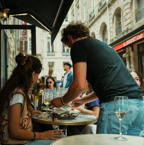 Un écailler de Dimanch'Huîtres servant un plateau d'huîtres fraîches à des clients installés sur une terrasse animée dans le centre-ville de Bordeaux. Service traiteur de la mer et animation iodée haut de gamme pour des événements privés et professionnels en Gironde.