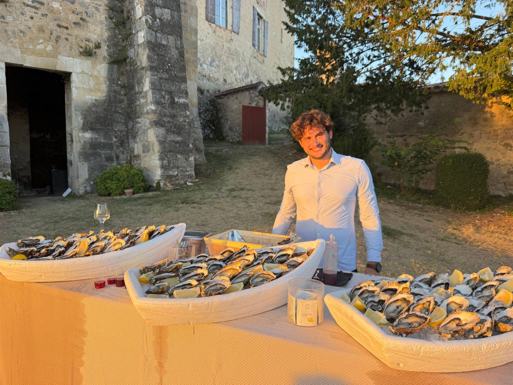Écailler Dimanchuitres souriant derrière ses barques d'huîtres devant un château en Gironde